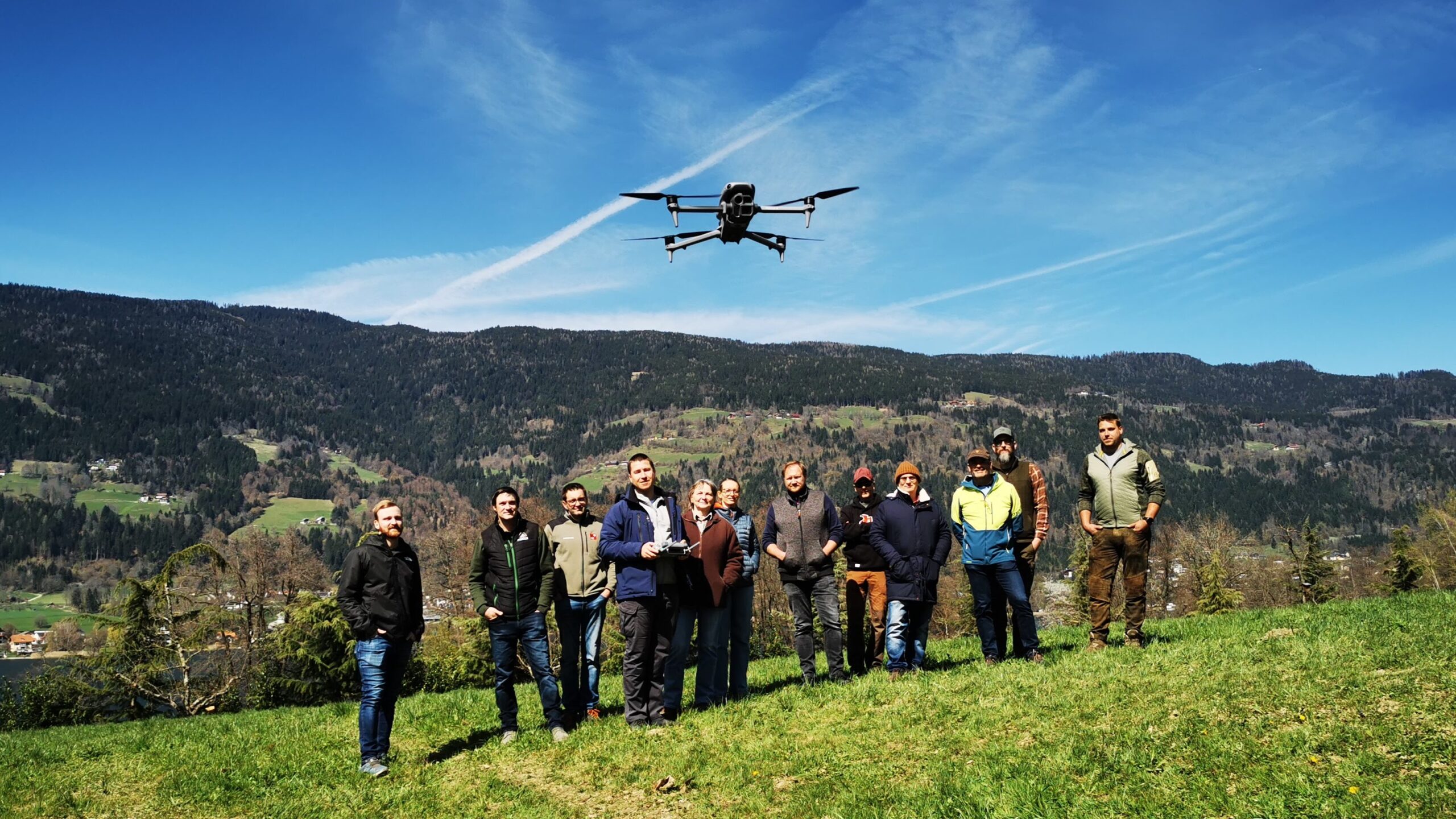 Mehrere Personen stehen auf einer Wiese und über ihnen fliegt eine Drohne.